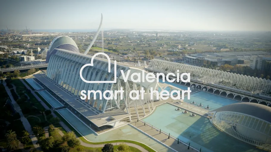 Vista a&eacute;rea de un edificio moderno y unas piscinas en Valencia, Espa&ntilde;a, con el campo al fondo. El texto superpuesto en blanco reza: &laquo;Valencia smart at heart&raquo;, con un dise&ntilde;o en forma de coraz&oacute;n sobre las palabras.